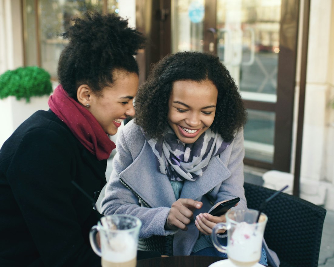 Two women laughing over lattes at a cafΓ© table