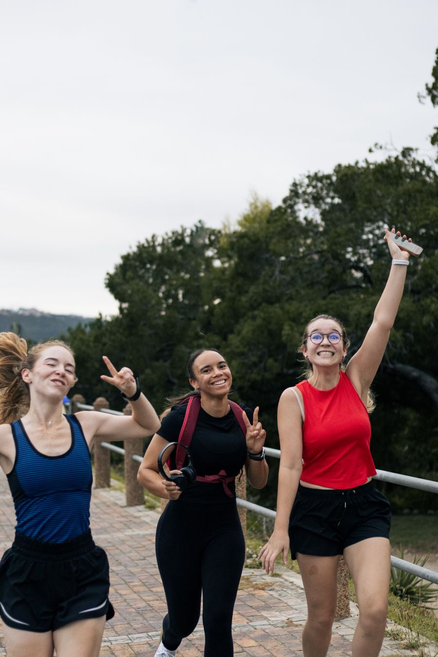 Three friends in activewear laughing and making peace signs on a walking path